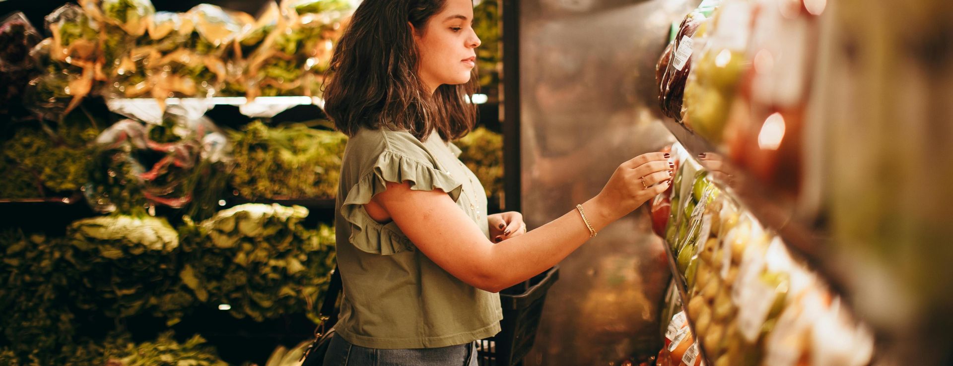 A woman selecting fresh vegetables from a supermarket aisle.